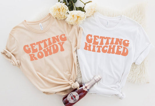 Beige short sleeve t-shirt with getting rowdy written on the front in peach and a white short sleeve t-shirt with getting hitched written in peach on the front. 